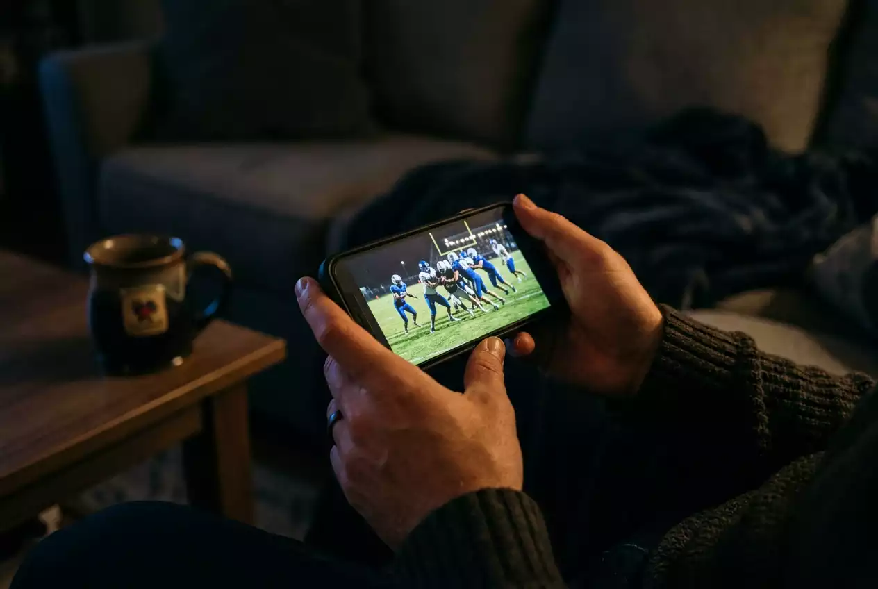 Person watching an NFL game on a smartphone screen in a dimly lit room at night